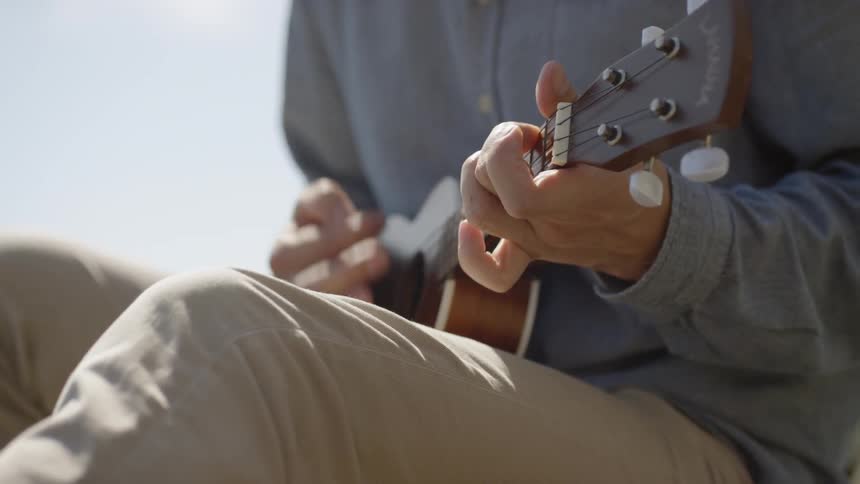 A man is smiling and playing a guitar outdoors