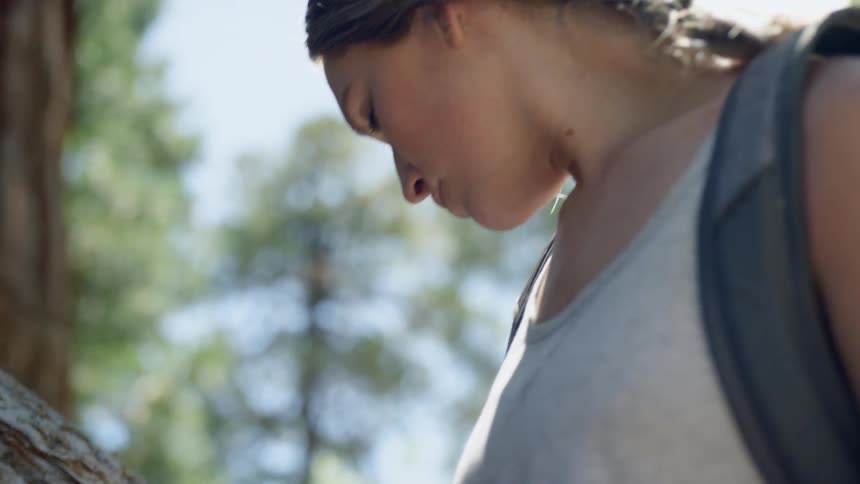 A woman leans on a tree branch outside