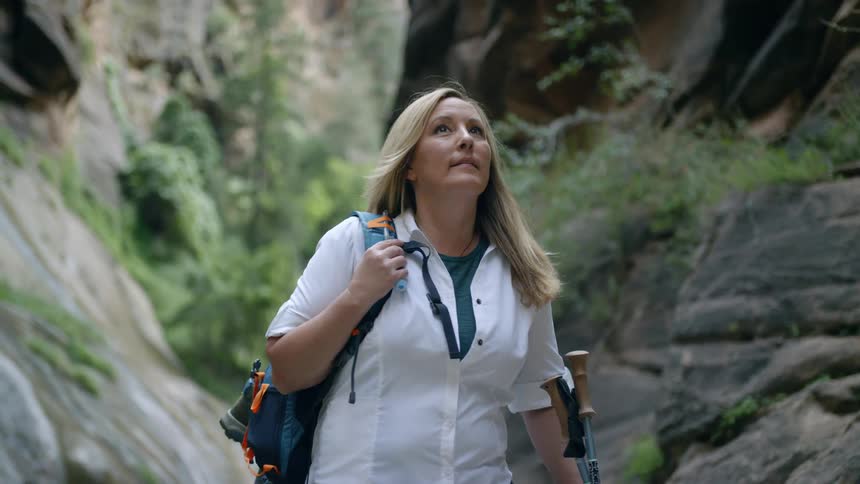 A blonde haired woman stands outdoors surrounded by rocks as she looks up at her surroundings