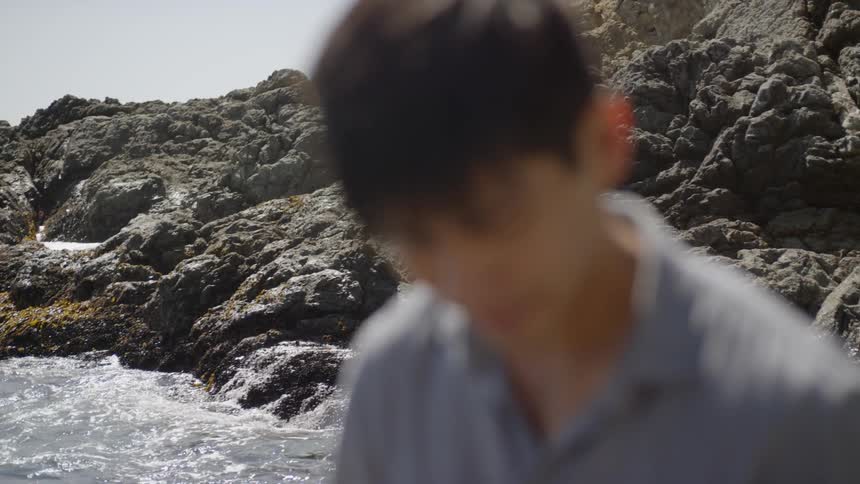 An asian man standing on a rocky coastline