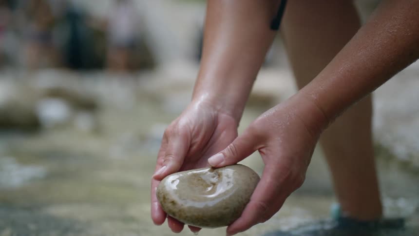A man stands in a shallow creek and rubs a large rock