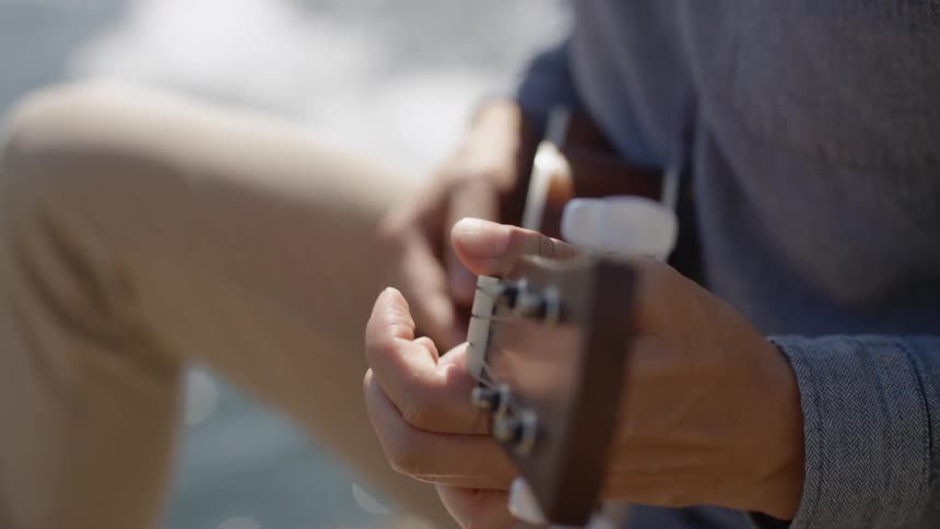 A man sits outside and plays a ukulele