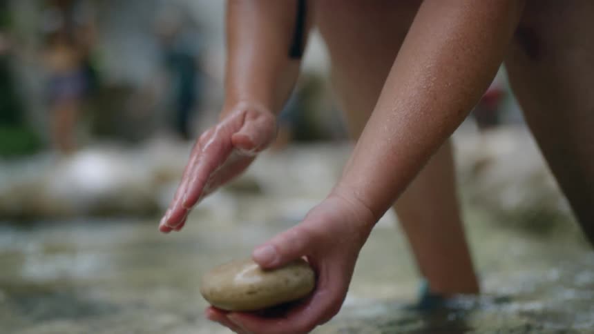 A woman picks a rock up out of the water