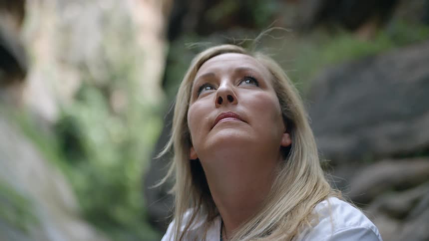 A blonde haired woman in a wilderness area looks up