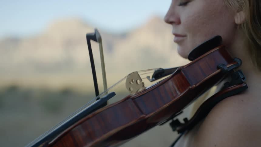 A woman standing playing a violin with the sky in the background