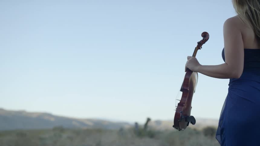 A woman carries a violin through a desert landscape