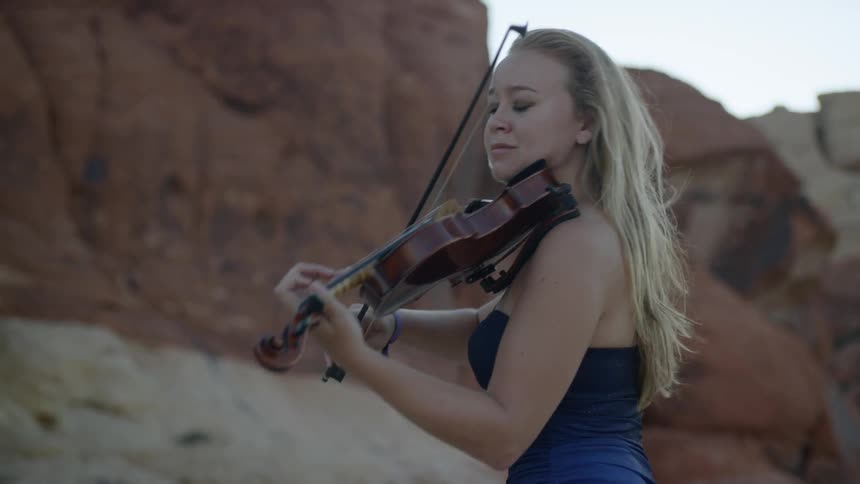 Female with long blonde hair playing violin in a canyon