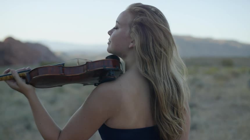 Blonde woman plays on the violin in the canyon in the late afternoon