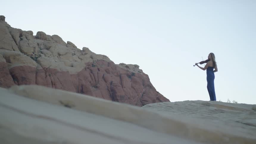 A woman plays the violin while standing on a tall mountain top