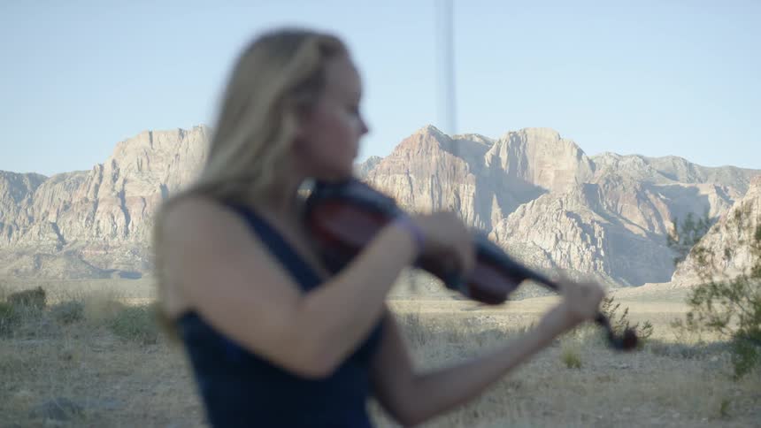An older white woman plays a violin outdoors
