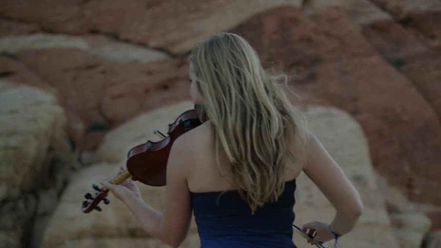A woman is playing her violin near a towering rocky surface