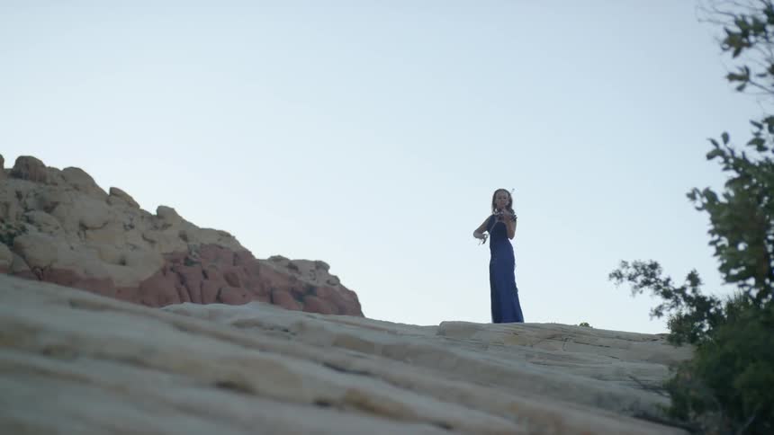 Woman in a long dress playing violin on a plateau in the canyon