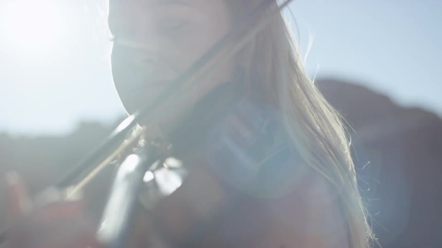 Blonde woman plays on the violin while the sun beams