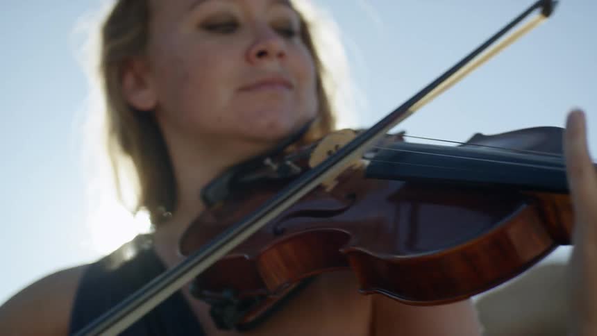 A blonde woman plays a violin outdoors