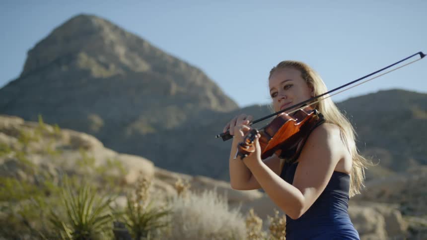 A woman plays violin outside near a mountain range