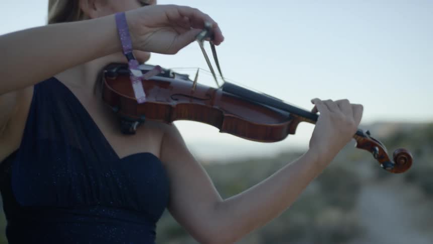 An older white woman plays a violin while standing outdoors