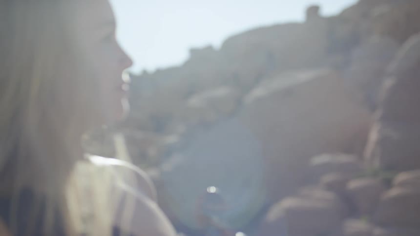 A blonde woman stands outdoor looking around while holding a violin