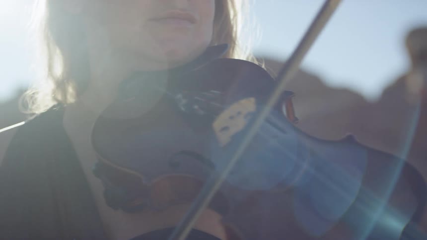 A white female is outside playing the violin with the suns rays beating down on her