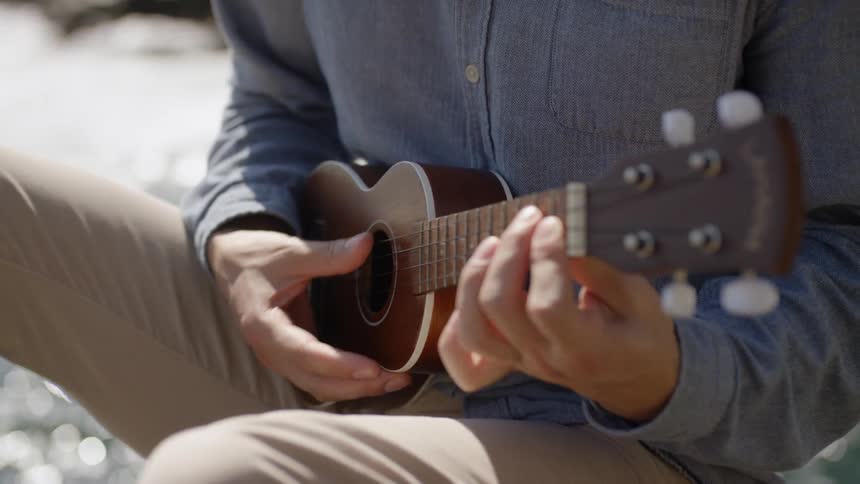 Man sitting down on the rock plays a ukulele next to the river
