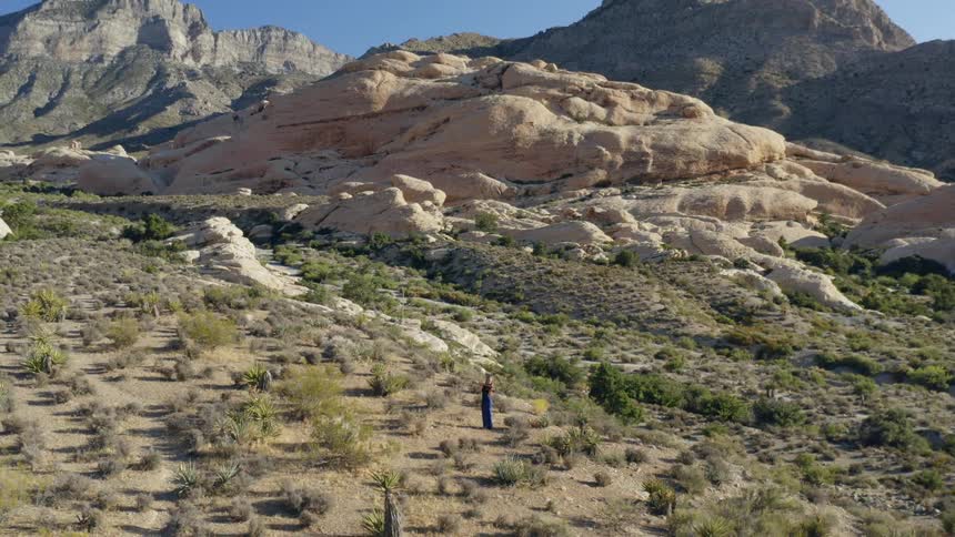 A woman stands in the middle of a mountain and dry terrain playing the violin