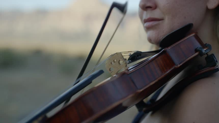 A woman stands outside and plays a violin
