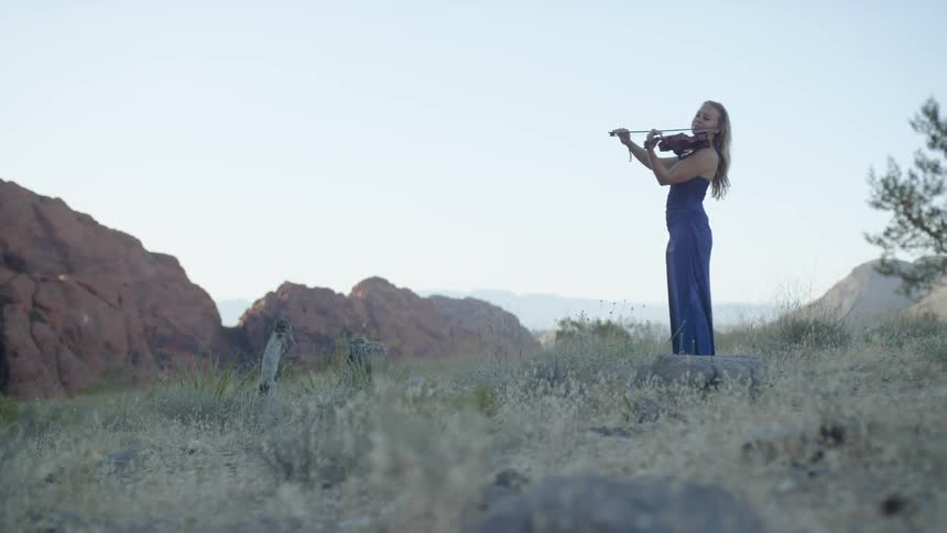 Woman plays violin outdoors in field near rock outcropping