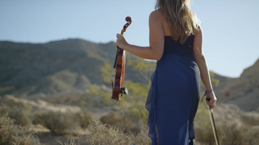 A young girl walks outside while carrying a violin