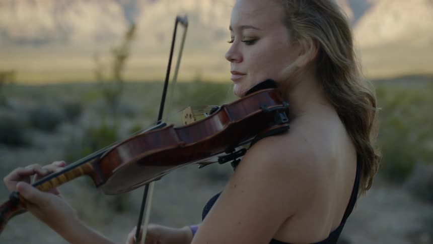 Woman plays violin outside at sunrise in front of mountains