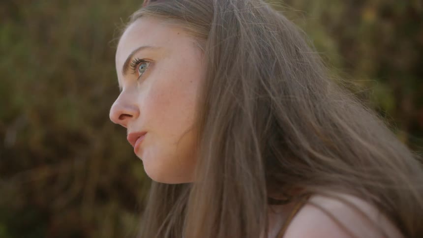A young woman sits outdoors and looks upwards in a pensive manner