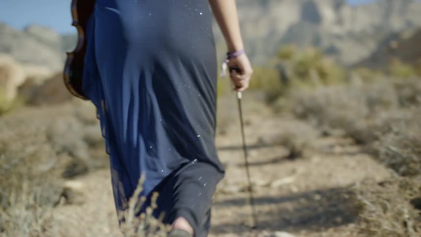 A woman is hiking in the desert with a violin