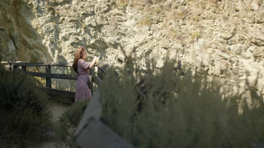 Woman in dress leaning on railing and writing on notebook