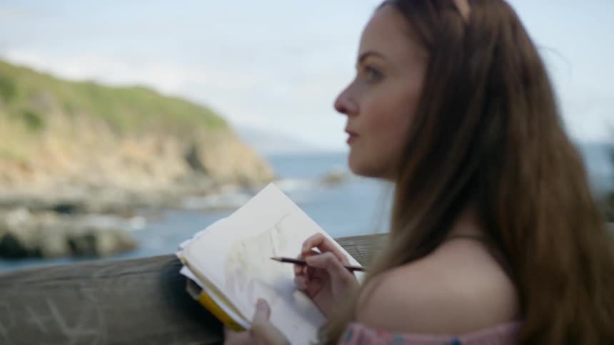 A woman is drawing a picture by the shore