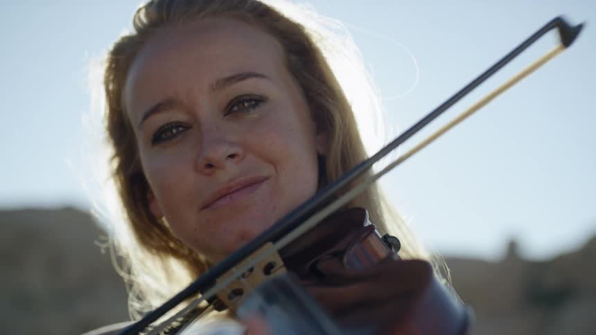 A woman playing a violin outdoors on a sunny day