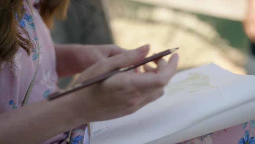 Ayoung girls takes out a colored pencil and starts to draw in a book