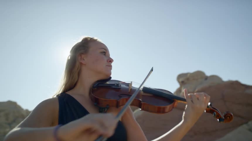 A woman plays a violin outside on a sunny day