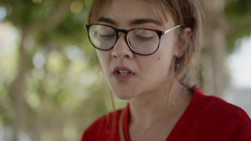 A young white woman puts on glasses while sitting at a table outdoors