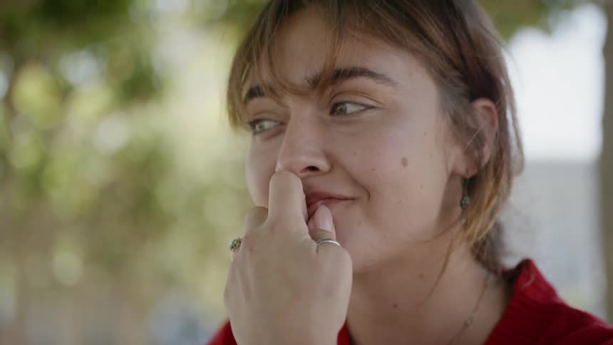 A white man sits outdoors and holds her hand up to her face