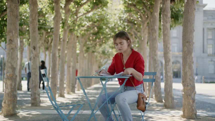 A woman is sitting outside writing a note