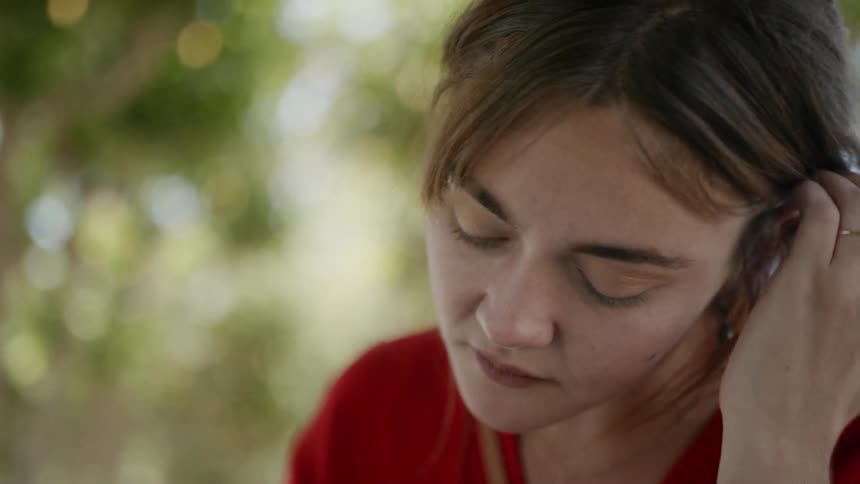 A woman tucks her hair behind her ear as she sits outside and writes in a journal