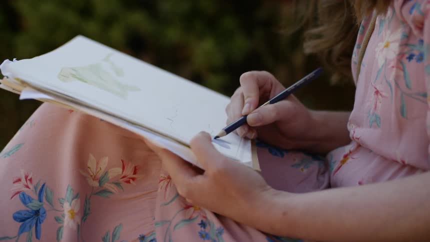 A woman sitting outside drawing on a pad