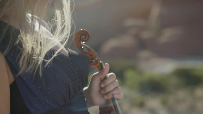 A blonde woman holding a violin stands outdoors