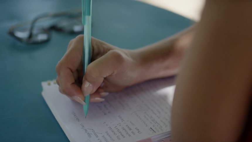 Woman sitting on table outdoors writes notes with pen on notepad