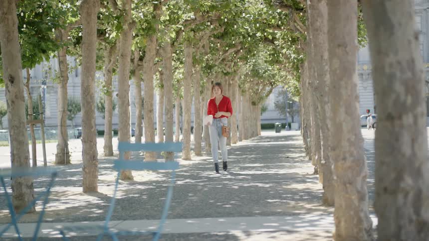 A young woman walks along a city walkway lined by rows of trees