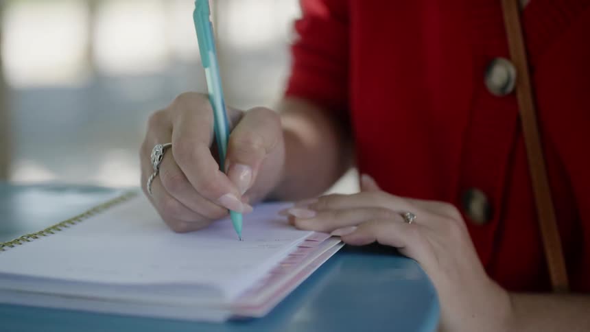 A woman is writing in a notebook with a blue pen