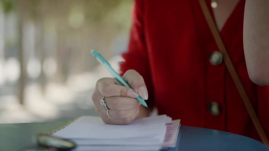 Woman writes in notebook while sitting at table outdoors