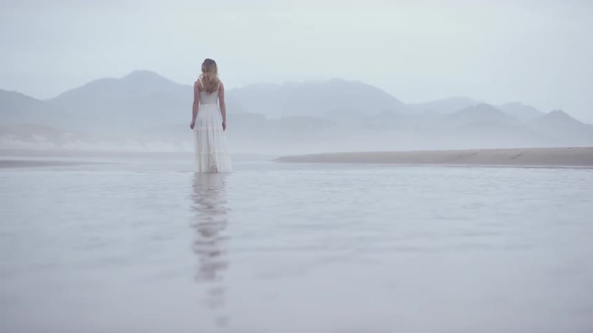 A woman stands in the water by the shore