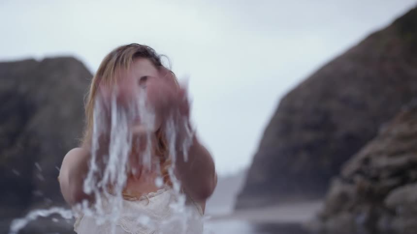 A woman on the beach smiling and splashing water