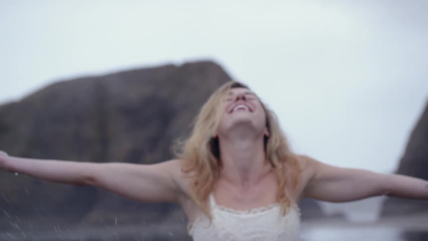 On a cloudy day a young woman tosses water into the air on a rocky beach