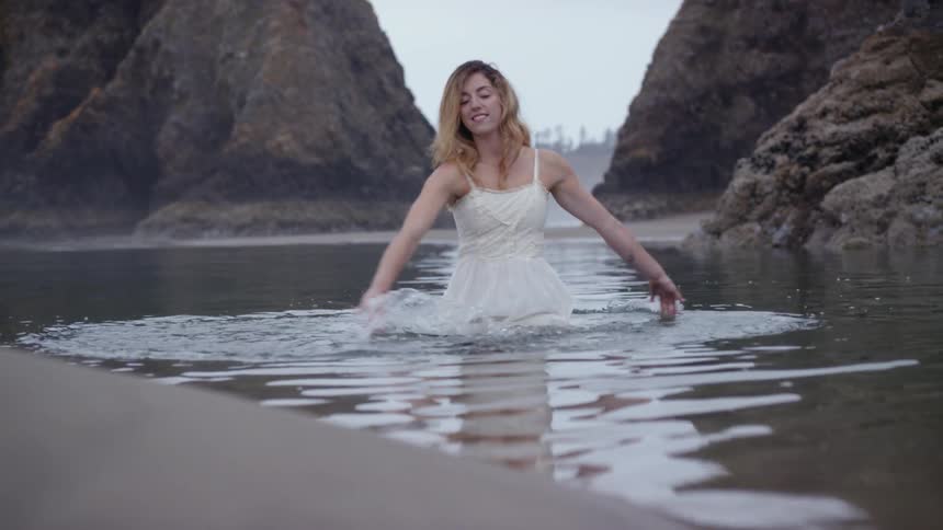 A woman is standing in the water by cliffs