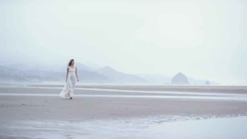 A woman in a white dress is walking on the beach
